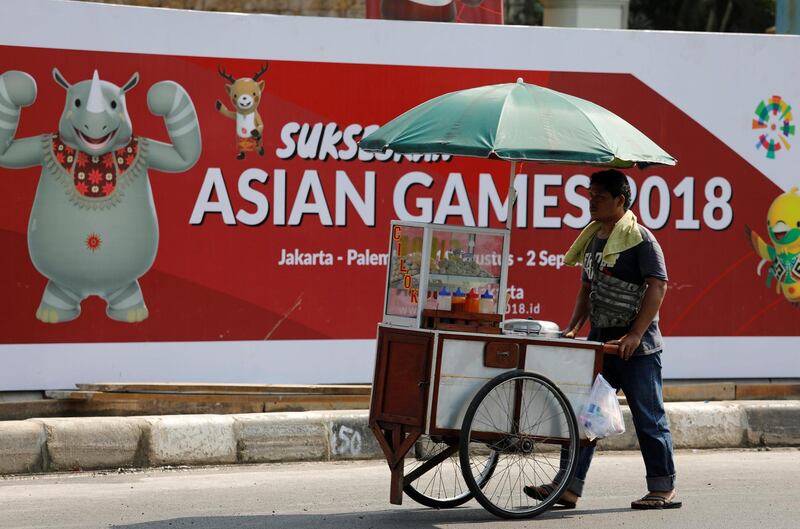 A food vendor pushes his cart past a sign promoting the upcoming Asian Games, to be held in Jakarta and Palembang, on a main road in Jakarta, Indonesia July 15, 2018. REUTERS/Darren Whiteside