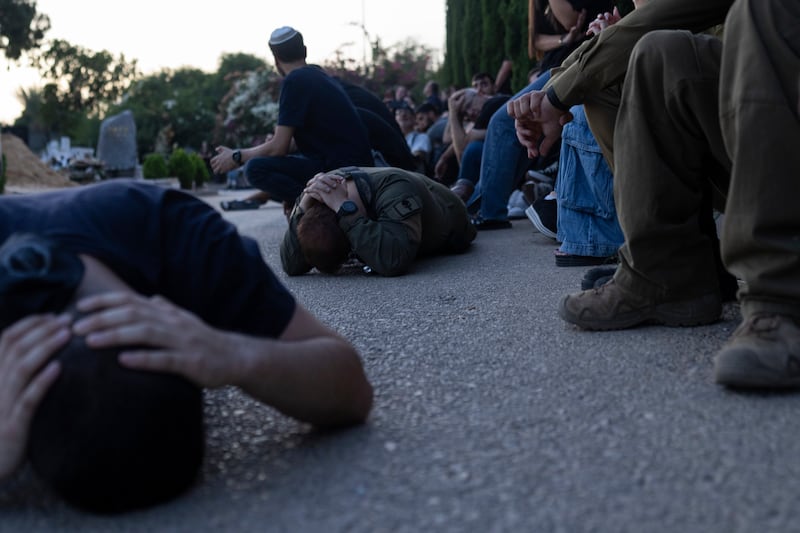 Israelis at a cemetery in Holon during a funeral take cover as a siren warns of incoming rockets fired from the Gaza Strip. AP