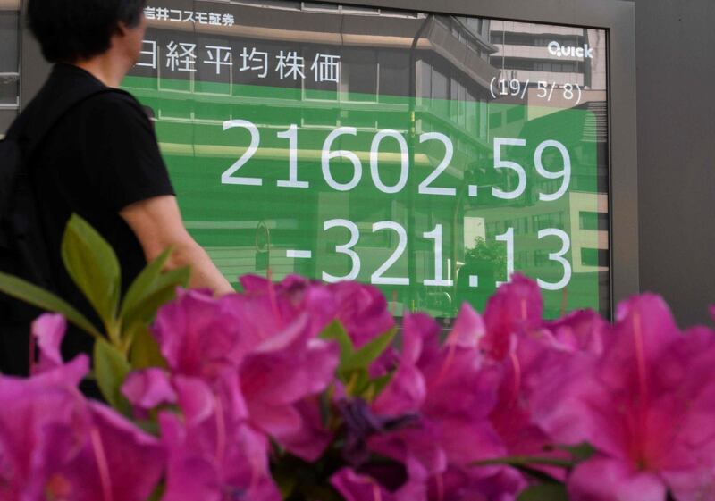 A pedestrian walks past an electronics stock indicator in the window of a securities company in Tokyo displaying the closing numbers for the Tokyo Stock Exchange on May 8, 2019. Tokyo stocks closed lower on May 8, as fears about a US-China trade war and a higher yen against the dollar weighed on the market. / AFP / Toshifumi KITAMURA
