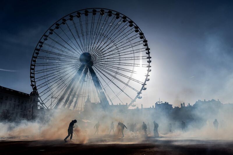 People stand amid tear-gas smoke during a demonstration in Lyon as part of the sixth day of massive strike action over government's plans to overhaul the pension system. AFP