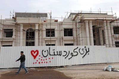 A man walks past a graffiti reading in Kurdish "Long live Kurdistan”, near the scene of a rocket attack in Arbil, the capital of the northern Iraqi Kurdish autonomous region, on February 16, 2021. The United Nations warned Iraq could spin out of control after a rocket attack on the Kurdish regional capital Arbil killed a foreign contractor and wounded several Iraqis and foreigners. / AFP / SAFIN HAMED
