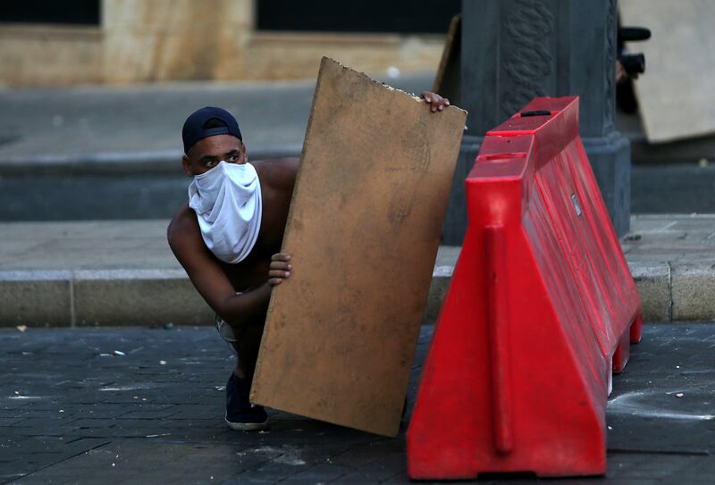 A protester uses a wooden board as cover during clashes with Lebanese army and security forces in Beirut, on the first anniversary of the blast that ravaged the port and the city. AFP