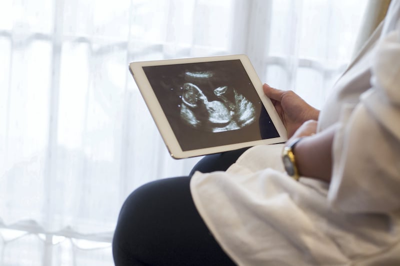 Lower Section of a pregnant woman holding a digital tablet and showing an ultrasound image of her unborn baby side by side with her pregnant belly.