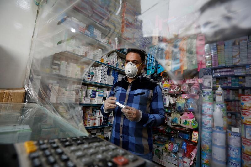 A pharmacist wearing a protective face mask serves his customers behind a plastic shield installed as a precautionary measure against the spread of the coronavirus in Sanaa, Yemen, on May 19, 2020. EPA