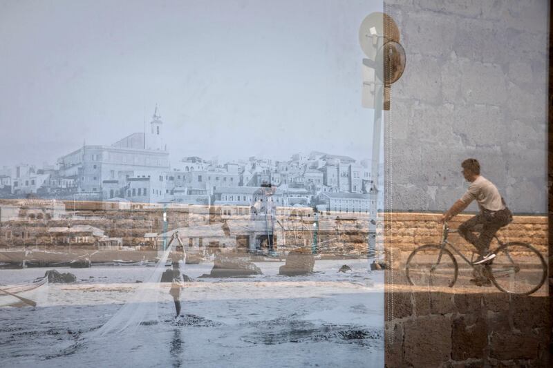 A man riding his bicycle is reflected on an old picture of Jaffa displayed in a window, in the Jaffa neighborhood of Tel Aviv, Israel. AP Photo