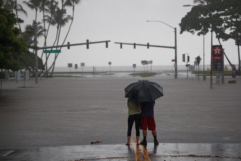 People share a moment under an umbrella, as they view the flooded Pauahi St and Kamehameha Ave intersection in Hilo, Hawaii. EPA
