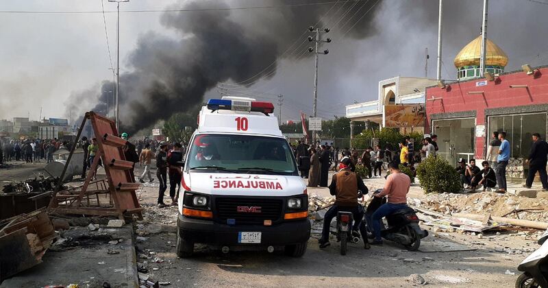 An ambulance drives past people taking part in a protest as smoke rises from a burning military truck after clashes between protesters and Iraqi policemen in Nasiriyah city, some 370km southeast of Baghdad, Iraq.  EPA