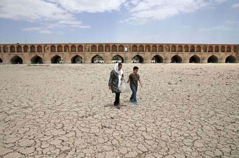 A woman and a boy walk on the dried up riverbed of the Zayandeh Roud river that no longer runs under the 400-year-old Si-o-seh Pol bridge, named for its 33 arches, in Isfahan, Iran, on July 10, 2018. AP Photo