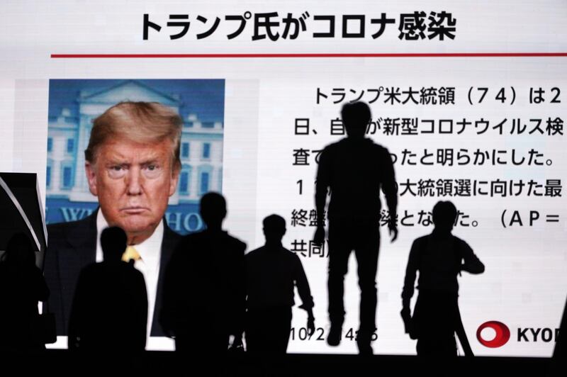 People walk past a screen showing the news report that US President Donald Trump has tested positive for the coronavirus in Tokyo, Japan. AP Photo