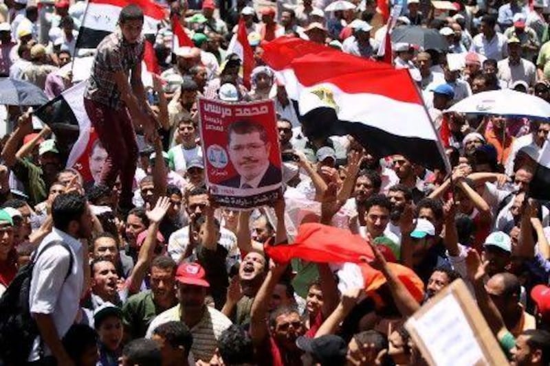 Egyptian supporters of the Muslim Brotherhood presidential candidate Mohammed Morsi hold his portrait and wave national flags during a demonstration in Cairo's Tahrir square yesterday.