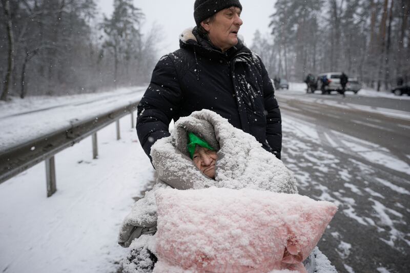 An elderly woman is coated in snow as she sits in a wheelchair after being rescued from Irpin. AP