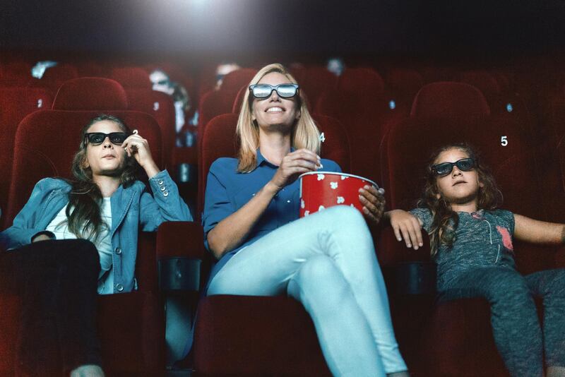 Closeup low angle view of a single mom watching a movie at a movie theater with her daughters. They are sitting in the front row, eating popcorn and wearing a 3d glasses.