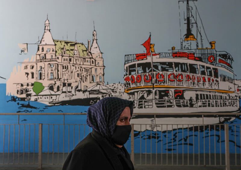 A woman wearing a face mask walks past a city-sponsored graffiti mural depicting the historical Haydarpasa Train Station (left) and the famous ferry (right) at a metrobus station in Istanbul, Turkey.  EPA