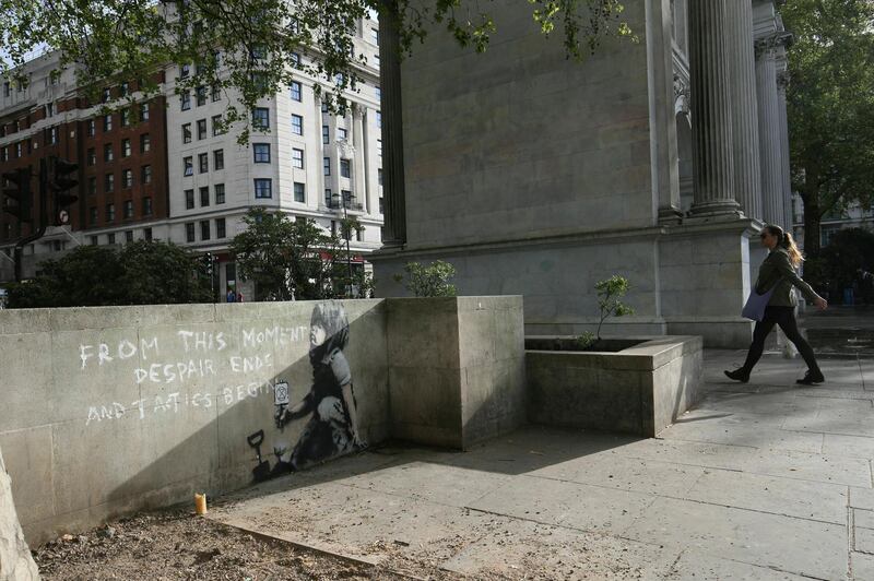 A woman walks nearby an artwork which appears to be by street artist Banksy. PA via AP