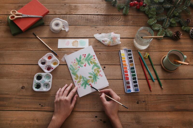 Young woman painting Christmas card with water colors, top view. Getty Images