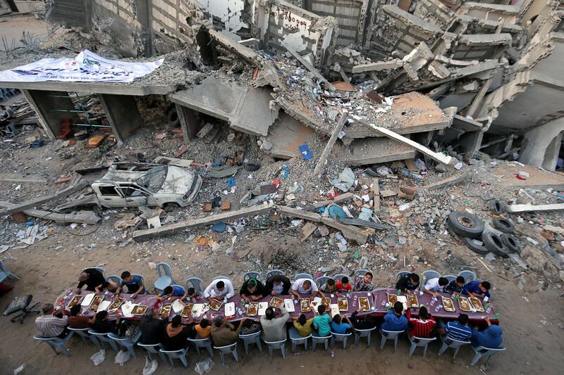 Palestinians break their fast by eating the Iftar meals during the holy month of Ramadan, near the rubble of a building recently destroyed by Israeli air strikes, in Gaza City.  Reuters