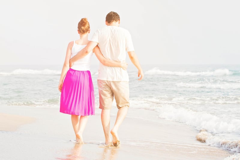 Young adult male and female holding hands on beach at sunset. Getty Images