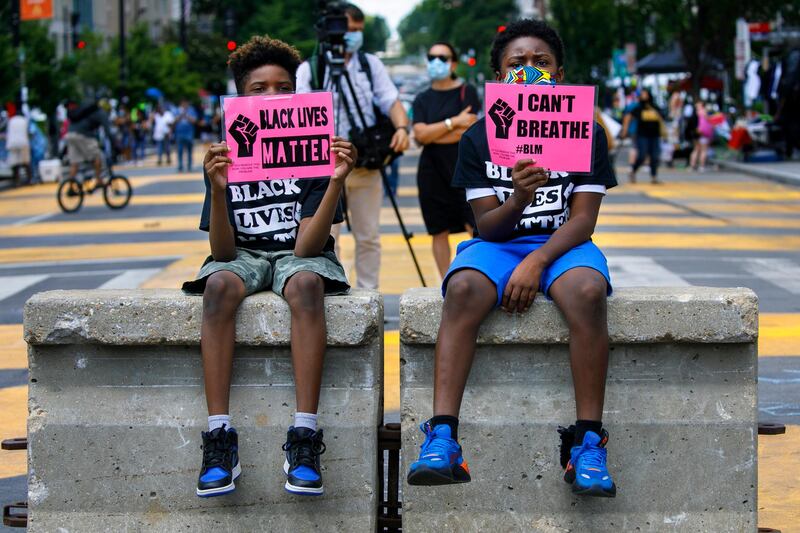 FILE - In this June 24, 2020, file photo, Tyshawn, 9, left, and his brother Tyler, 11, right, of Baltimore, hold signs saying "Black Lives Matter" and "I Can't Breathe" as they sit on a concrete barrier near a police line as demonstrators protest along a section of 16th Street that has been renamed Black Lives Matter Plaza in Washington. Thousands of Black activists from across the U.S. will hold the 2020 Black National Convention on Aug. 28, 2020, via livestream to produce a new political agenda that builds on the protests that followed George Floydâ€™s death. Organizers of the gathering shared their plans with The Associated Press on Wednesday, July 1, ahead of an official announcement. (AP Photo/Jacquelyn Martin, File)