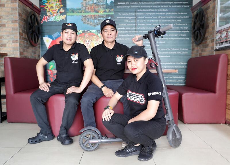 Abu Dhabi, United Arab Emirates, August 14, 2019.  E-scooter work mates at Bacolod Lechon Manok and Inasal, a Filipino grilled chicken spot at downtown Abu Dhabi take a quick break to pose infront of their ever faithful e-scooter.  (L-R0  Joylan Arcona, Perryl Malapitan and Sumaya Indog.
Victor Besa/The National
Section:  NA
Reporter:  Haneen Dajani