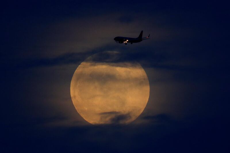 A full moon rises between clouds as a landing commercial jet approaches the airport before the start of a total lunar eclipse that is being called a 'Super Blood Wolf Moon' in San Diego, California. Reuters