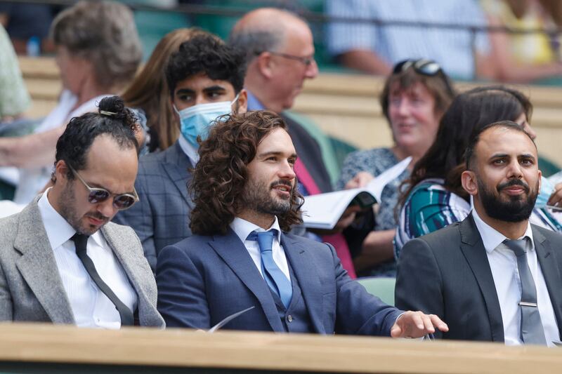 Fitness coach Joe Wicks, centre, sits as Tunisia's Ons Jabeur and Spain's Garbine Muguruza play their women's singles third round match on the fifth day of the 2021 Wimbledon Championships.