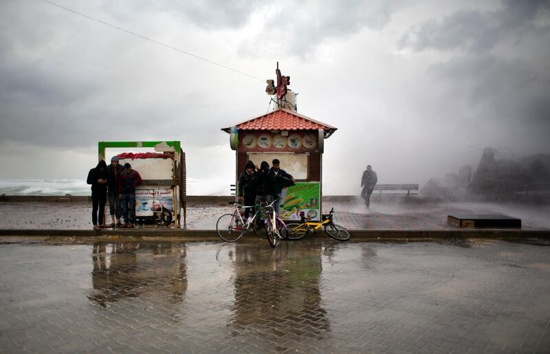 Palestinians take a cover from wind and rain on the Mediterranean seaside, in Gaza City, Wednesday, Jan. 16, 2019. A harsh weather front brought sandstorms, hail and rain to parts of the Middle East, with visibility down in the Egyptian capital as an orange cloud of dust blocked out the sky. Dusty winds whipped through Israel and the West Bank as well on Wednesday, with hail falling near Tel Aviv and meteorologists announcing that snow was expected later in the day in Jerusalem. (AP Photo/Khalil Hamra)
