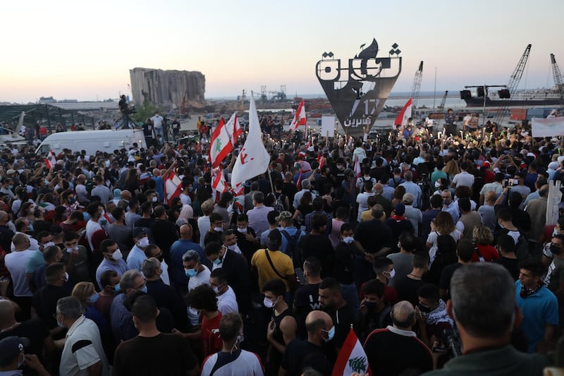 People wave Lebanese flags and chant to mark the first anniversary of anti-government protests with a background of the destroyed silos at Beirut port.  Getty Images