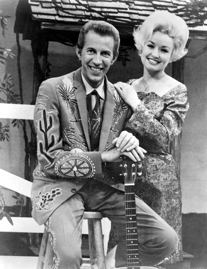 1967:  Country singer Dolly Parton with her collaborator Porter Wagoner on the set of his TV show in circa 1967. Mr. Wagoner is wearing a Nudie Suit designed by Nudie Cohn of Nudie's Rodeo Tailors. (Photo by Michael Ochs Archives/Getty Images)