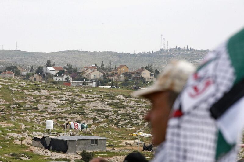 A Palestinian man takes part in a protest in the Palestinian village of Susya, south of Yatta town, in the occupied West Bank on March 14, 2021, against the visit of the Israeli Prime Minister to the Israeli settlement of Susya (background).  / AFP / HAZEM BADER
