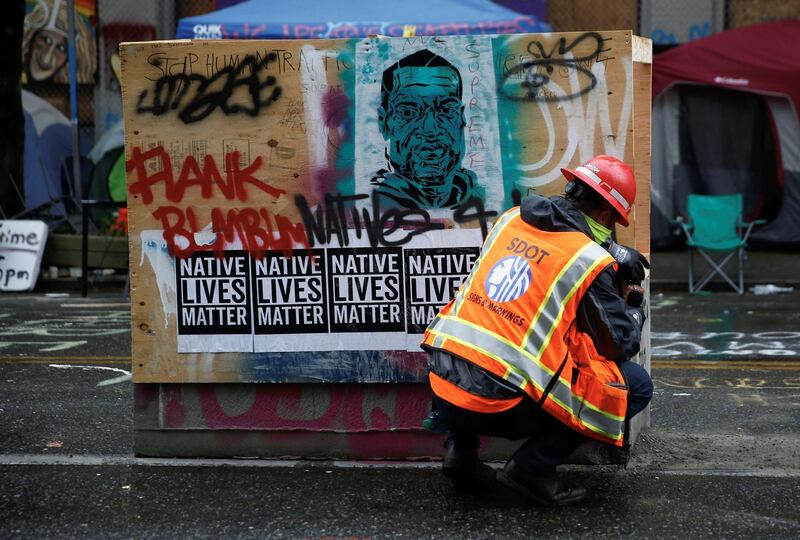 A Seattle Department of Transportation worker tears down plywood as Seattle Police maintain a perimeter while retaking the Capitol Hill Occupied Protest area. Reuters