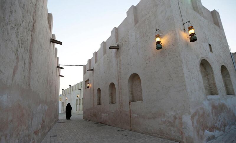An Emirati woman walks past traditional houses.