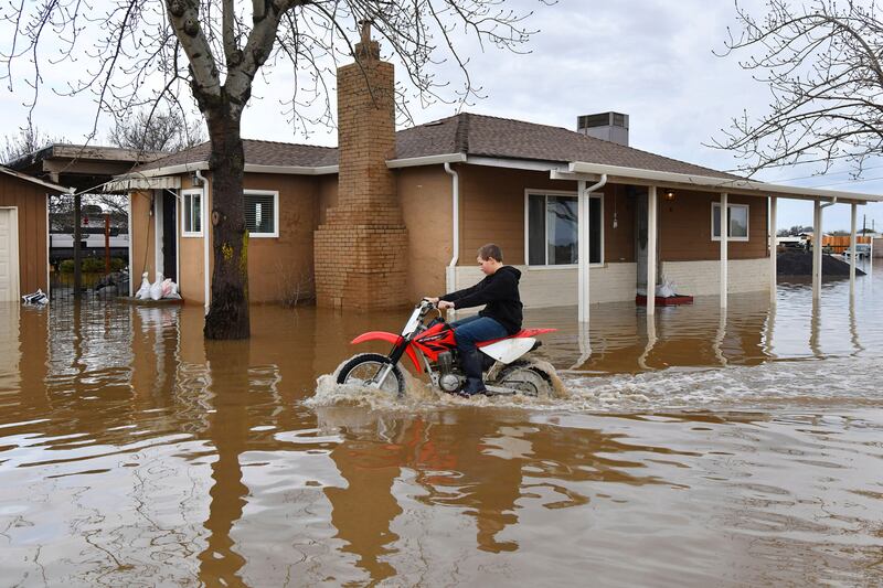 A child rides his off-road motorcycle around his flooded home in Brentwood. AP