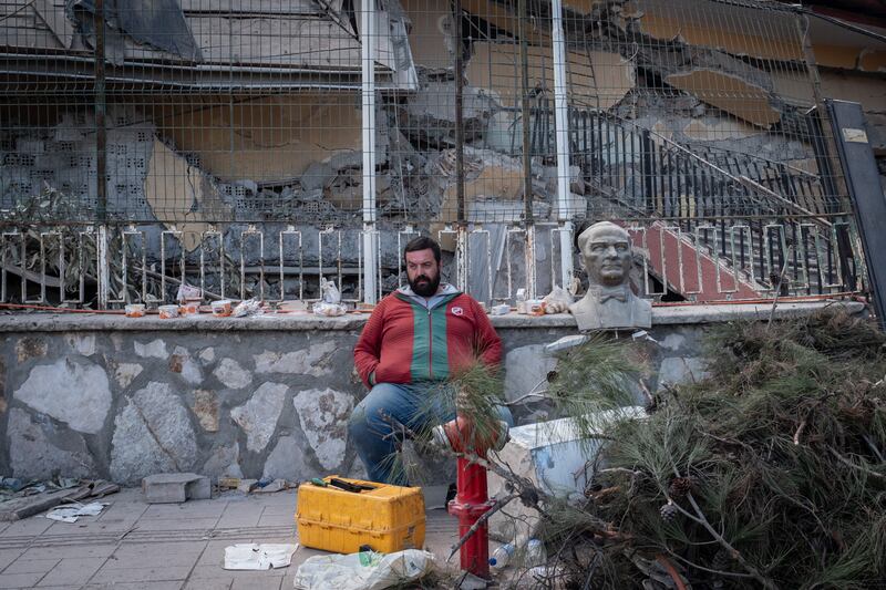 A man sits next to a bust of Turkey's founding father, Mustafa Kemal Ataturk, in front of collapsed buildings in Hatay, in Turkey. Getty