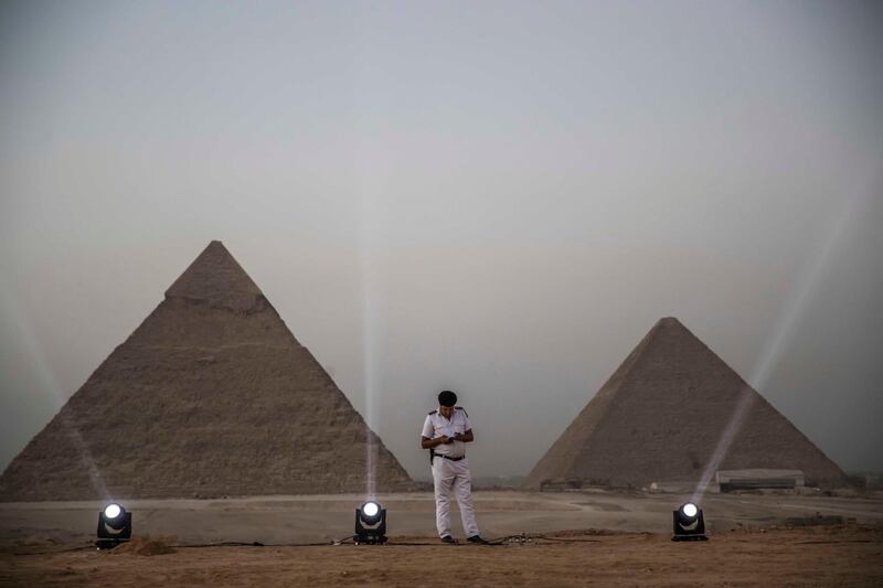 A policeman browses a phone while standing along a promontory overlooking (R to L) the Great Pyramid of Khufu (Cheops) and the Pyramid of Khafre (Chephren) at the Giza Pyramids necropolis on the southwestern outskirts of the Egyptian capital Cairo before an official ceremony launching the trial operations of the site's first environmentally-friendly electric bus and restaurant as part of a wider development plan at the necropolis.   AFP