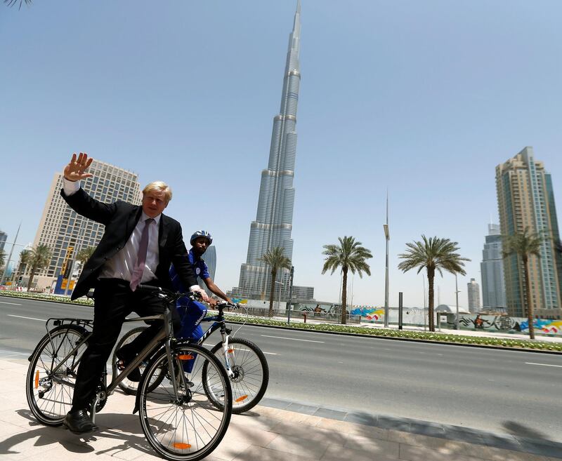 London mayor Boris Johnson salutes photographers as rides a bicycle in front of Burj Khalifa, the world's tallest tower, during his visit to Dubai, on April 16, 2013.  AFP PHOTO/KARIM SAHIB (Photo by KARIM SAHIB / AFP)