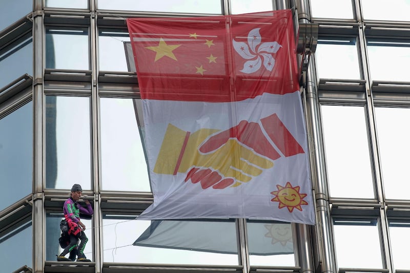 Alain Robert, known as the French Spider-Man, hangs a large fabric displaying Chinese and Hong Kong flags, shaking hands and shining sun at Cheung Kong Centre building in Hong Kong. AP Photo