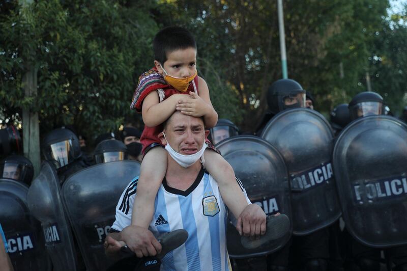 A man cries as he carries his child on his shoulders next to police blocking access to the Jardin de Bellavista cemetery during the funeral of Diego Maradona in Buenos Aires. AP