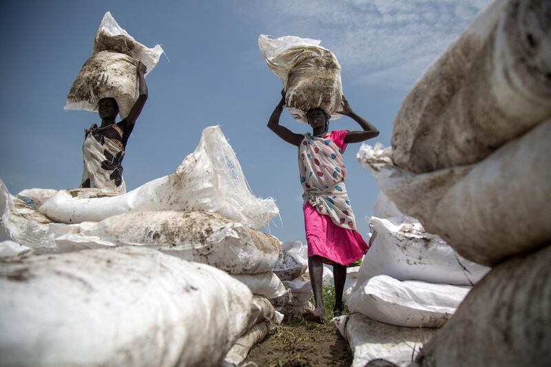 Women carry sacks of food, airdropped by the World Food Programme and distributed by the NGO Oxfam in Padding, near Lankien, Jonglei, South Sudan, on July 3, 2017. - Fighting between Government and opposition forces in April 2017 pushed thousands of civilians to be displaced in Padding and Lankien, both are still under opposition control. The massive displacement brought an outbreak of cholera and a serious need of health assistance, drinking water and food distribution among the population, according to the local leaders. (Photo by ALBERT GONZALEZ FARRAN / AFP)