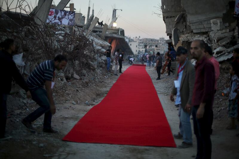 Palestinians place a red carpet between the ruins of houses, that witnesses said were destroyed by Israeli shelling during a 50-day war last summer, before they display a film on the war in the east of Gaza City May 12, 2015. REUTERS/Mohammed Salem