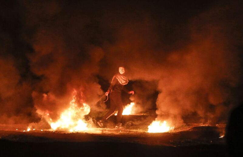 A masked Palestinian demonstrator pulls a burning tyre during a night demonstration near the fence along the border with Israel, east of Gaza City. AFP