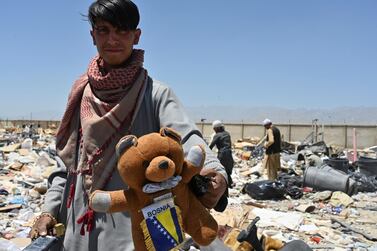 A man holds a teddy bear as people look for useable items at a junkyard near the Bagram Air Base in Bagram, June 17, 2021. AFP