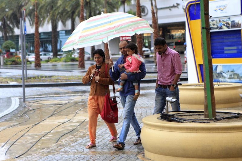 A family tries to take shelter under a large umbrella to avoid the rain at Jumeirah Beach Residence in Dubai. Sarah Dea/The National