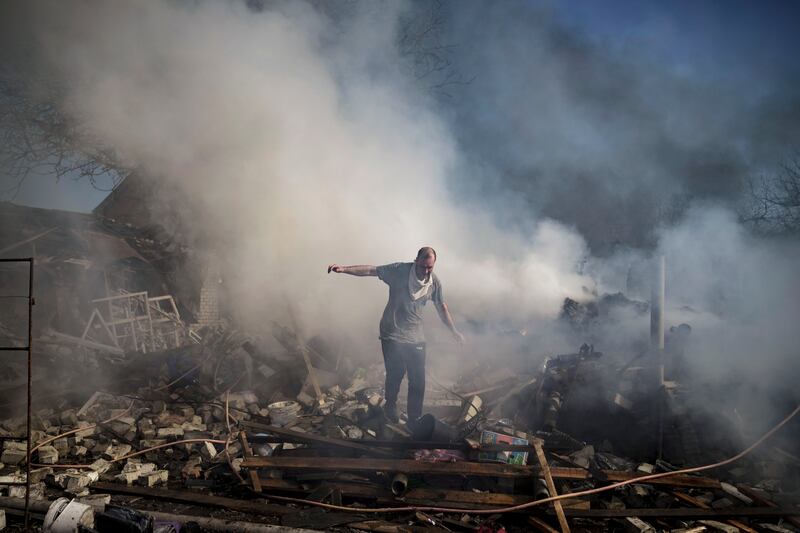A neighbour walks on the debris of a burning house destroyed in a Russian attack in Kharkiv, Ukraine. AP