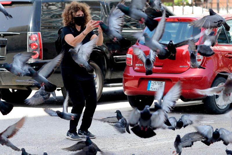 Lebanese director Carol Mansour uses her phone to film pigeons flying while wearing a face mask, in the centre of the capital Beirut. AFP