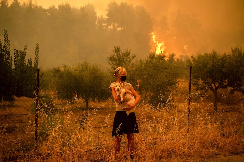 A woman cradles a dog as fires approach the village of Pefki, on Evia.