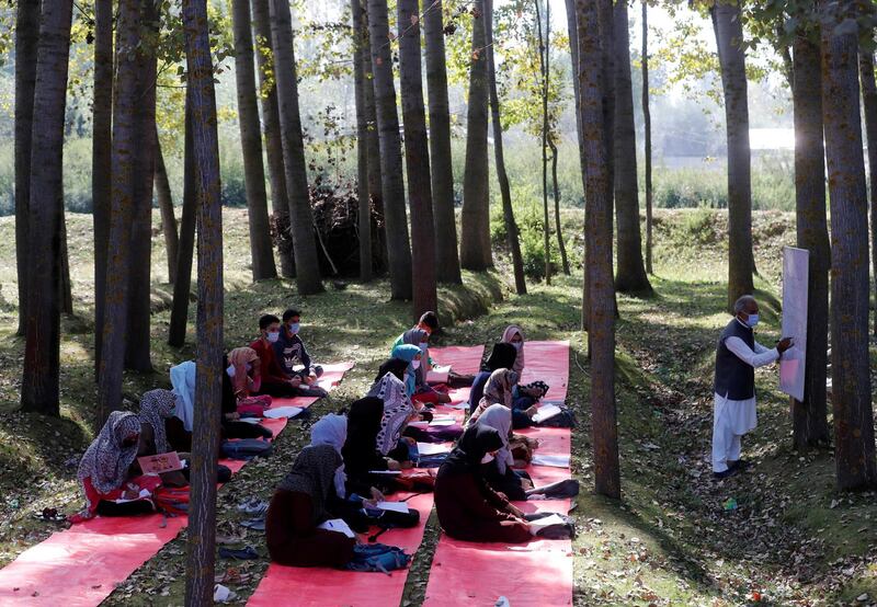 Students wearing protective face masks attend their class under the trees as they maintain social distancing outside their school in Gund on the outskirts of Srinagar. Reuters
