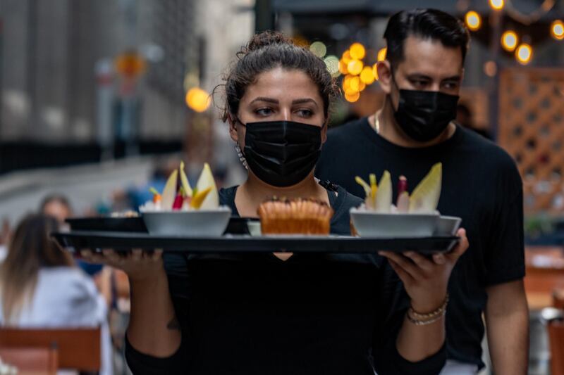 A worker wears a protective mask while carrying a tray with food in the outside dining area of Crown Shy restaurant in New York, U.S., on Saturday, Sept. 26, 2020. New York City currently prohibits all indoor dining, but will allow restaurants to open indoor dining rooms at 25% capacity, beginning September 30. Photographer: David 'Dee' Delgado/Bloomberg