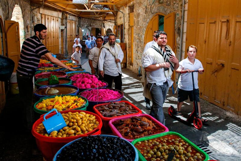 Jewish settlers guarded by Israeli security forces walk past a Palestinian pickled vegetable and olive vendor's stall as they tour the Palestinian side of the old city market in the occupied West Bank city of Hebron, during the Muslim holy fasting month of Ramadan on June 1, 2019.  / AFP / HAZEM BADER
