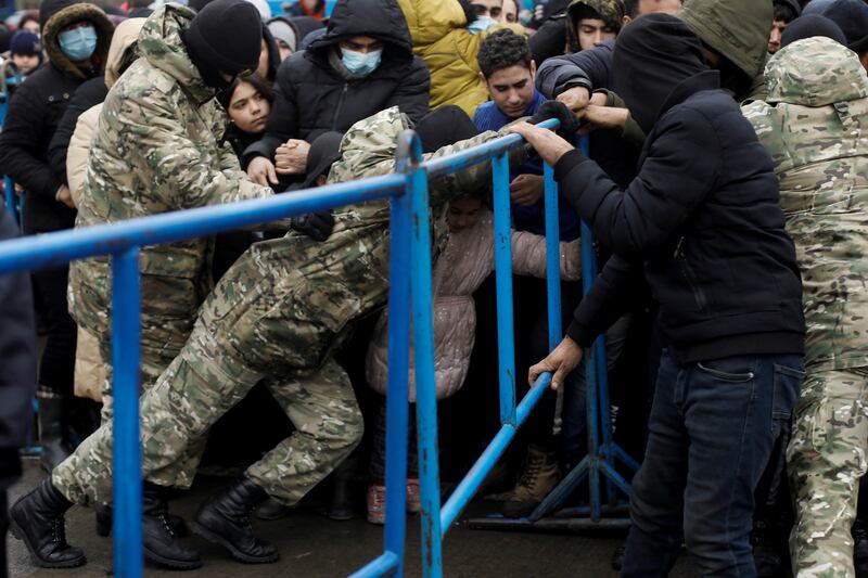 Belarusian servicemen hold a barrier as migrants jostle to receive food outside the transport and logistics centre near the border in the Grodno region. Reuters