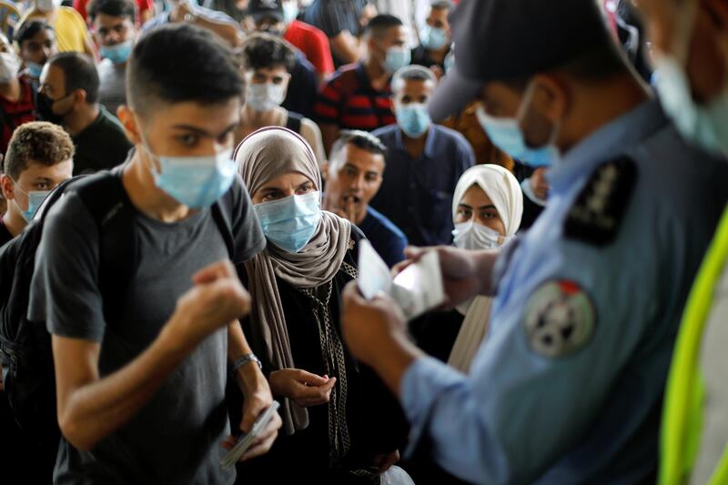 People wearing protective face masks have their documents checked by a police officer as they wait to leave the Palestinian Rafah border crossing with Egypt in the southern Gaza Strip. Reuters